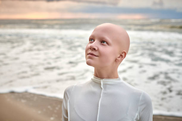 Close up portrait of young hairless girl with alopecia in white futuristic costume on sea background stock photo
