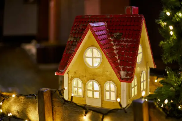 Photo of Christmas fairy tale house with warm glow windows at nighttime city street, symbolizes spirit