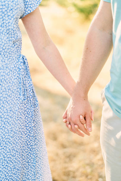 istock Husband holds his wife hand while standing in a sunny field. Cropped. Faceless 1948108455