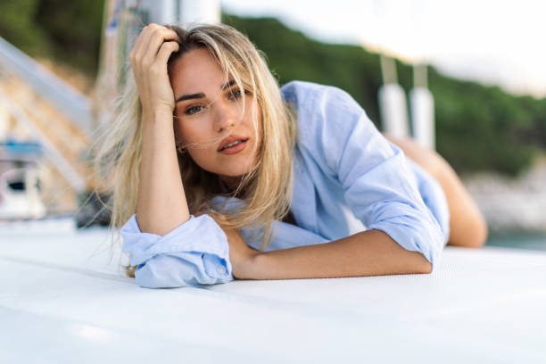 A beautiful young blond woman lying on a sailboat deck, she is looking relaxed, enjoying the moment