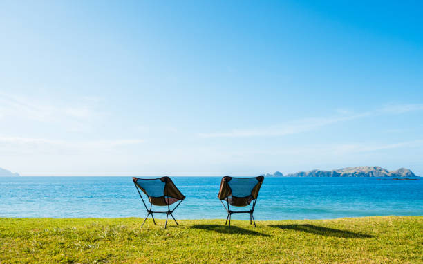 Two camping chairs facing towards beach on a sunny day with blue sky in Northland, New Zealand.