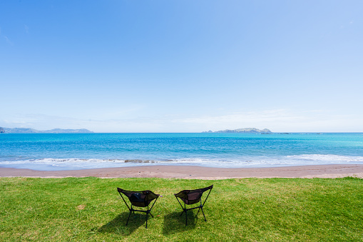 Two camping chairs facing towards beach on a sunny day with blue sky in Northland, New Zealand.