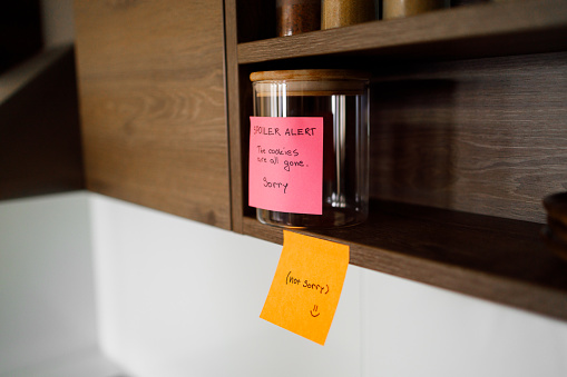 A humorous note is attached to an empty cookie jar on a wooden shelf, reading \