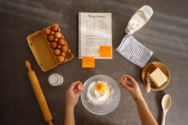 A woman is rolling dough in a bright kitchen, with a cookbook open to a croissant recipe, creating a scene of culinary dedication mixed with a touch of family affection.