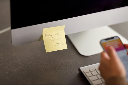 A close-up of a well-organized desk with a computer monitor, a sticky note with a reminder for 