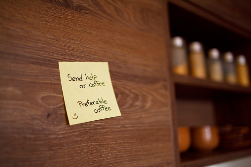 A sticky note on a wooden cabinet with a humorous plea, \