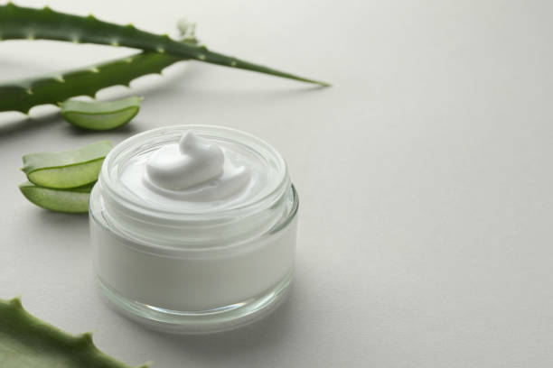 istock Jar with cream and cut aloe leaves on light grey background, closeup. Space for text 1948191774