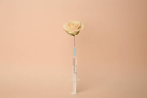 Medical syringe and rose flower on beige background
