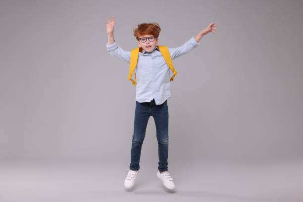 istock Happy schoolboy with backpack jumping on grey background 1948254720