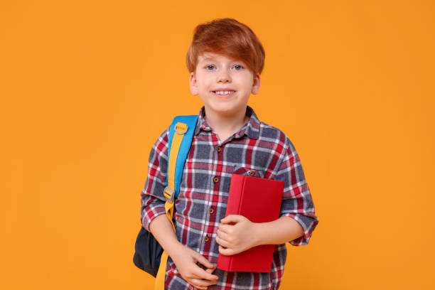 istock Happy schoolboy with backpack and book on orange background 1948257922
