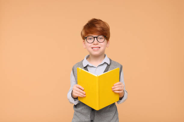 istock Smiling schoolboy with book on beige background 1948260033