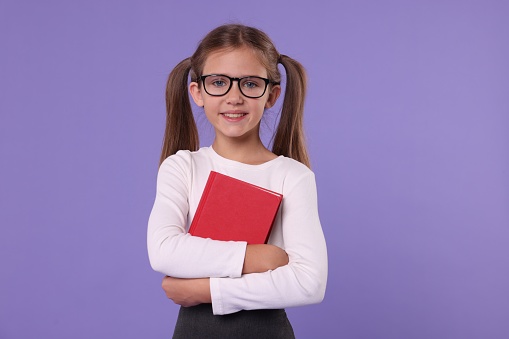 Smiling schoolgirl with book on violet background