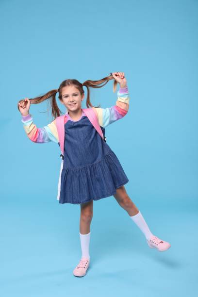 istock Happy schoolgirl with backpack on light blue background 1948269590