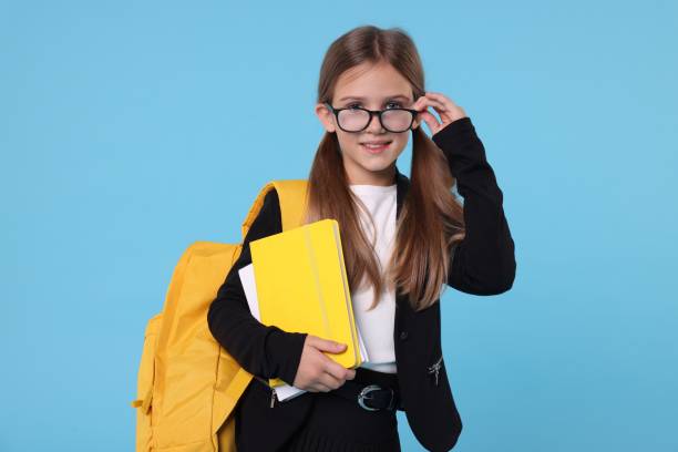 istock Happy schoolgirl with backpack and books on light blue background 1948269612