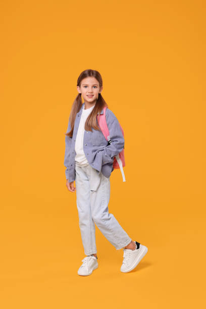 istock Happy schoolgirl with backpack on orange background 1948272262