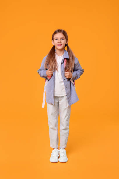 istock Happy schoolgirl with backpack on orange background 1948274854