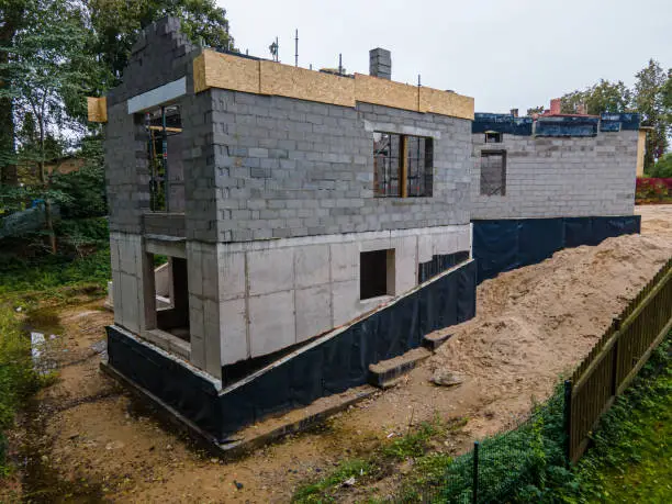 Progress on a suburban home construction site with exposed cinder block walls and wooden roof beams