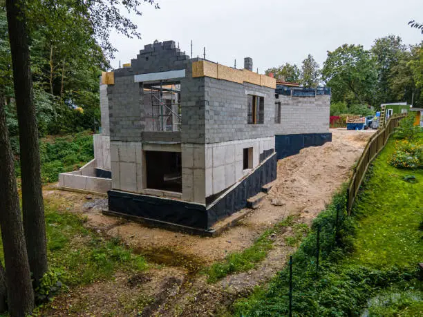 Progress on a suburban home construction site with exposed cinder block walls and wooden roof beams