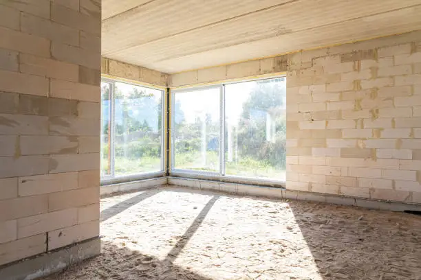 Sunlit corner of a room in an under-construction house with exposed concrete blocks and large windows