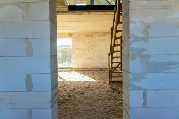 Sunlit corner of a room in an under-construction house with exposed concrete blocks and large windows