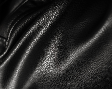 Black leather with waves and folds. Textured background of faux or eco leather, vegan artificial fabric on PVC base. Close up of texture, macro.
