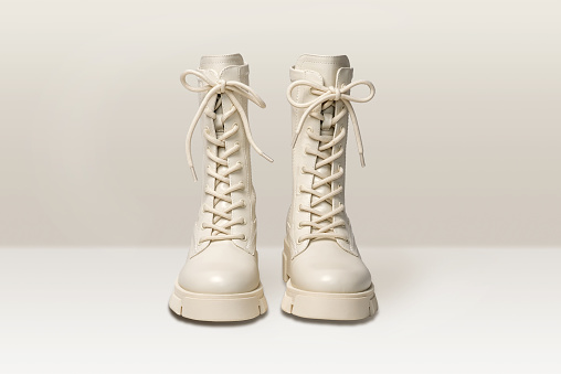 Pair of stylish white boots for women on light gray background. Trendy military beige boots on high platform with laces. Female fashion and shoes still life. Front view.