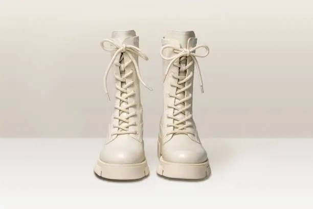 Photo of Pair of stylish white boots for women on light gray background. Trendy military beige boots on high platform with laces. Female fashion and shoes still life. Front view