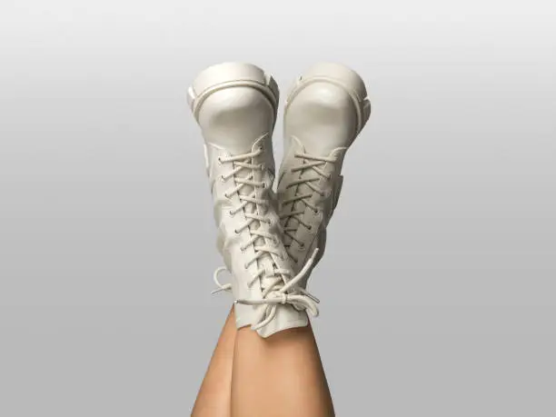 Photo of Crossed female legs in white combat boots upside down isolated on white gray background. Woman wearing trendy military beige shoes on high platform with laces. Seasonal female fashion