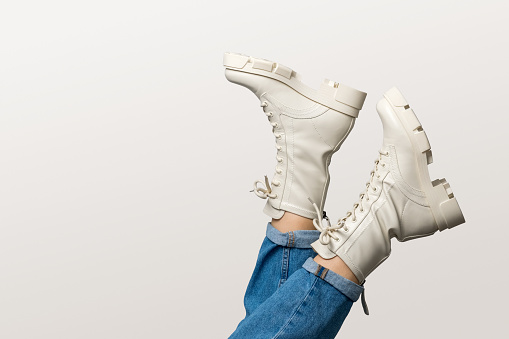Female legs in white combat boots and blue jeans upside down on white background, side view. Woman wearing trendy military beige shoes on high platform with laces. Seasonal female fashion.