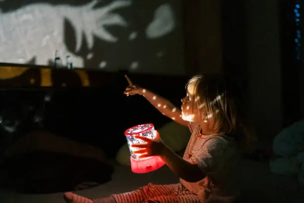 Little girl with a night-light projector in her hand points to the picture on the wall. High quality photo