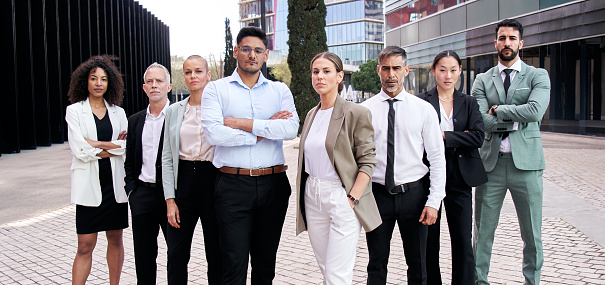 Team portrait diverse professional posing confidence. Young and mature multiracial colleagues looking serious at camera crossing arms outdoor. Group successful office workers standing in formal attire