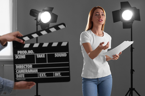 Casting call. Emotional woman performing while second assistance camera holding clapperboard against grey background in studio