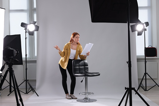 Casting call. Emotional woman with script performing on grey background in modern studio