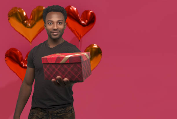 hombre sosteniendo la caja de regalo sobre fondo rosa con globos en forma de corazón para la tarjeta del día de san valentín con espacio de copia - balloon pink black anniversary fotografías e imágenes de stock