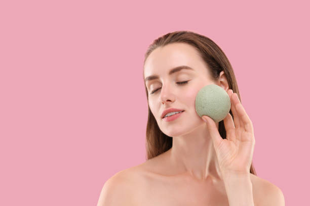 istock Young woman washing her face with sponge on pink background. Space for text 1948397628