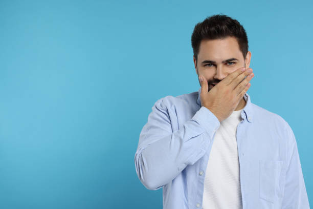 istock Embarrassed man covering mouth on light blue background. Space for text 1948436821