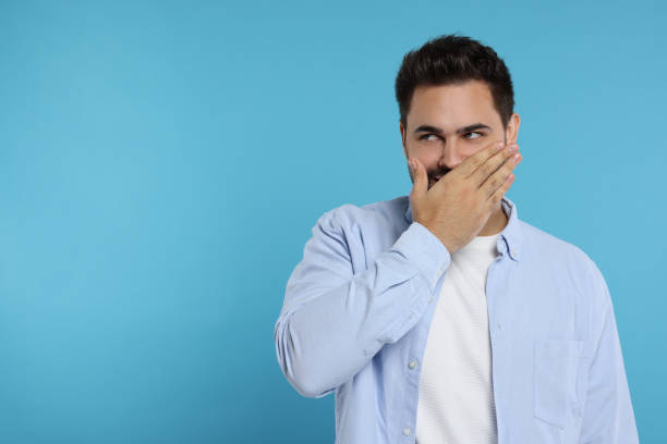 istock Embarrassed man covering mouth on light blue background. Space for text 1948438350