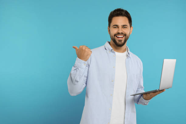 istock Special promotion. Smiling man with laptop pointing at something on light blue background. Space for text 1948444693