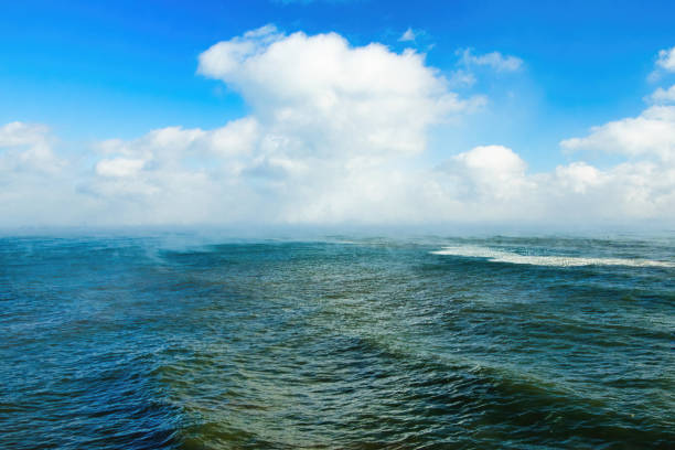 Landscape view of gentle waves on Lake Michigan beneath fluffy clouds and fog on a Winter day.