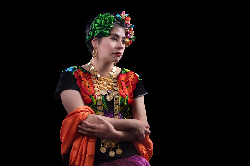 Mexican Latin woman dressed in the traditional costume of the isthmus region in Oaxaca in Mexico, embroidered with multi-colored flowers, necklaces of golden coins and braids on her head