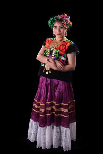 Mexican Latin woman dressed in the traditional costume of the isthmus region in Oaxaca in Mexico, embroidered with multi-colored flowers, necklaces of golden coins and braids on her head