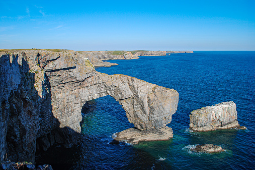 Natural rock arch known as The Green Bridge of Wales on the coast of Pembrokeshire, UK. Blue water and cliff landscape