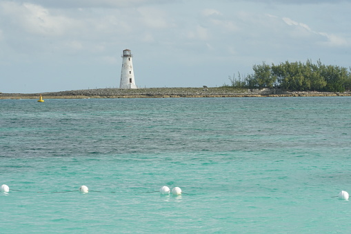 Entrance to Nassau harbour in the Bahamas with old white lighthouse on a breakwater at the one of the islands in the Caribbean Sea, captured at sunny day during  winter season.
