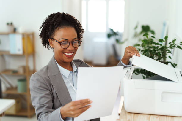 young smiling businesswoman using printer at the office - printer computer printer computer document ストックフォトと画像