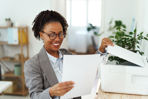 Young smiling businesswoman using printer at the office