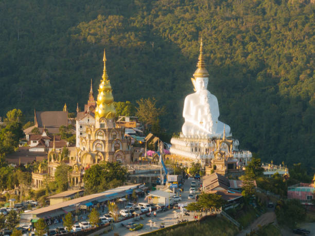 istock The setting sun illuminates a striking white Buddha statue beside an ornate temple, with a lively street scene unfolding below 1948663865
