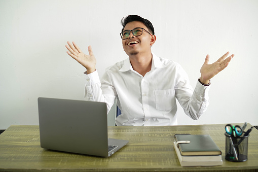 young asian businessman in a workplace smiling a lot with open both arms, wearing white shirt with glasses isolated