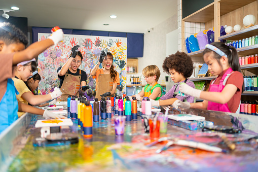 Group of Diversity school children learning acrylic pouring art on canvas workshop with teacher at art studio. Happy boys and girls enjoy and fun with colorful abstract modern art painting in classroom.