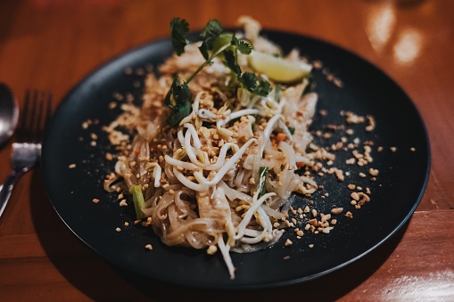 A delectable close-up of the famous Thai dish Pad Thai, served in an inviting restaurant. The detailed shot showcases perfectly cooked noodles with fresh ingredients, enhanced by exotic spices and artistically garnished. A feast for the senses, capturing the authentic taste and culinary diversity of Thailand