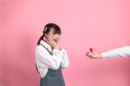 Asian senior man and woman couple in overalls casual clothing with  gesture of surprise for Receiving an Engagement Ring isolated on pink background. St Valentine's Day, Women's Day, Birthday